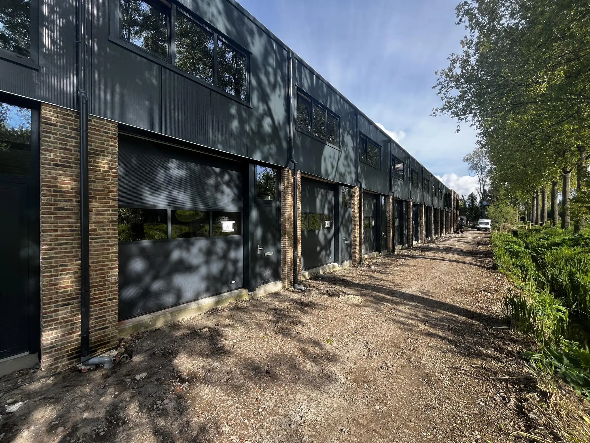 Rij moderne bedrijfsunits aan de Broekdijk West 19-4 met onverharde weg en bomenrij.